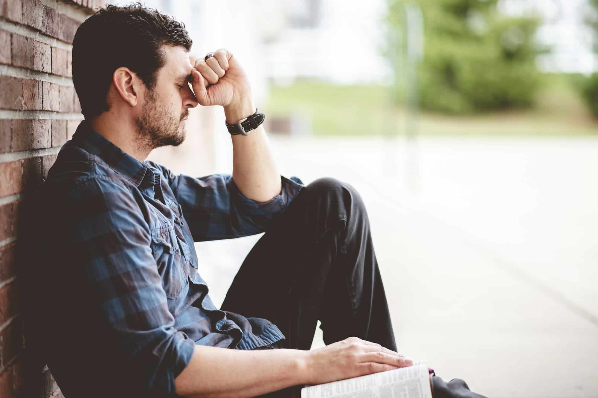 Lonely depressed person sitting near a brick wall with the Bible on his lap