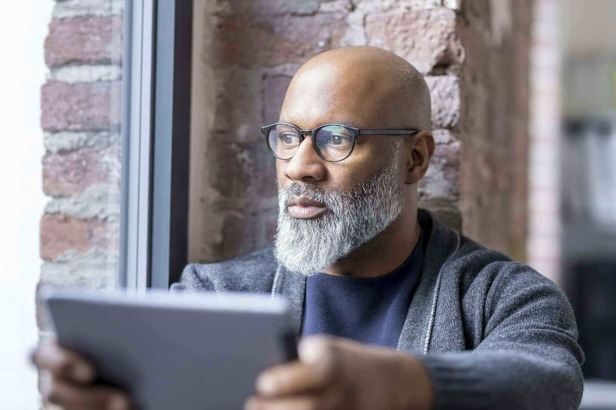 Portrait of pensive man with tablet looking out of window