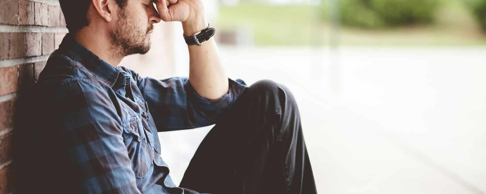 Lonely depressed person sitting near a brick wall with the Bible on his lap